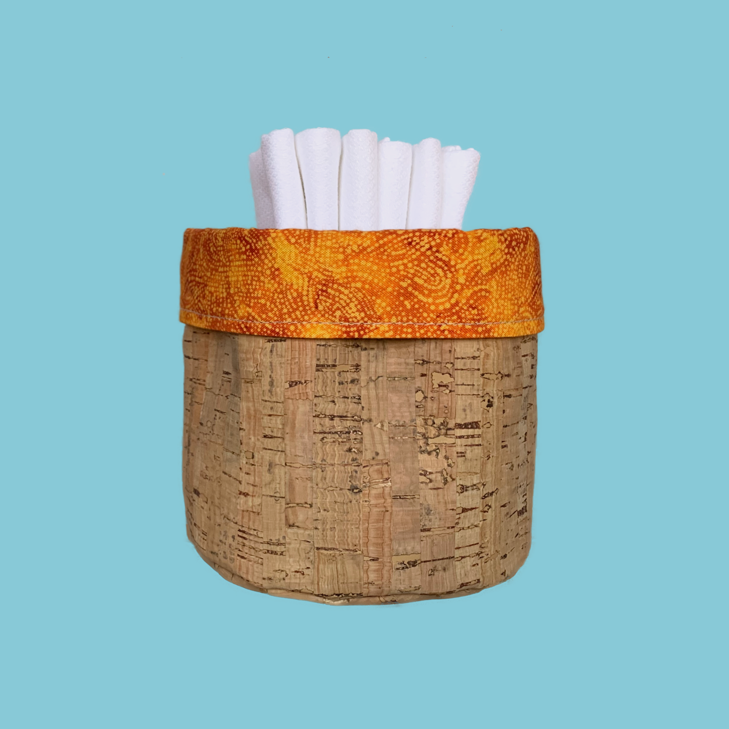 Orange Batik and Cork Fabric Basket that is reversible. It is holding six unpaper towels