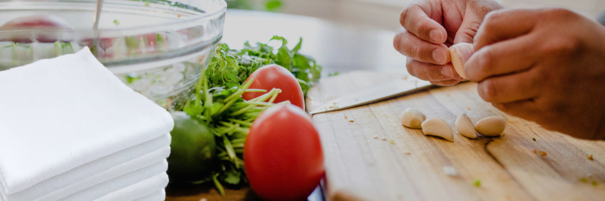 Cutting board with person cutting garlic. Handecloth reusable paper towels on he side
